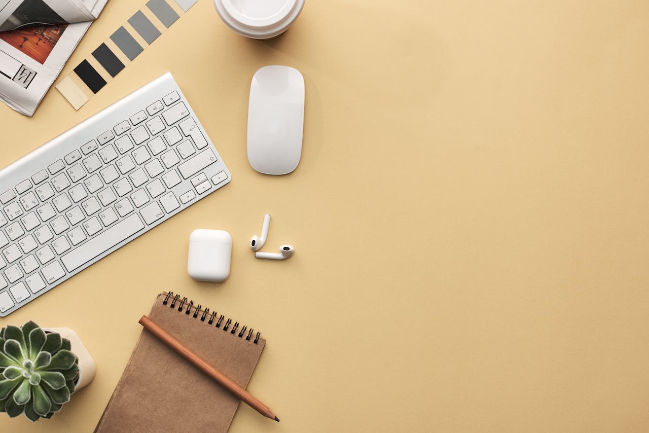 who-we-are A minimalist workspace flat lay with keyboard, mouse, notebook, and succulent on a beige background.